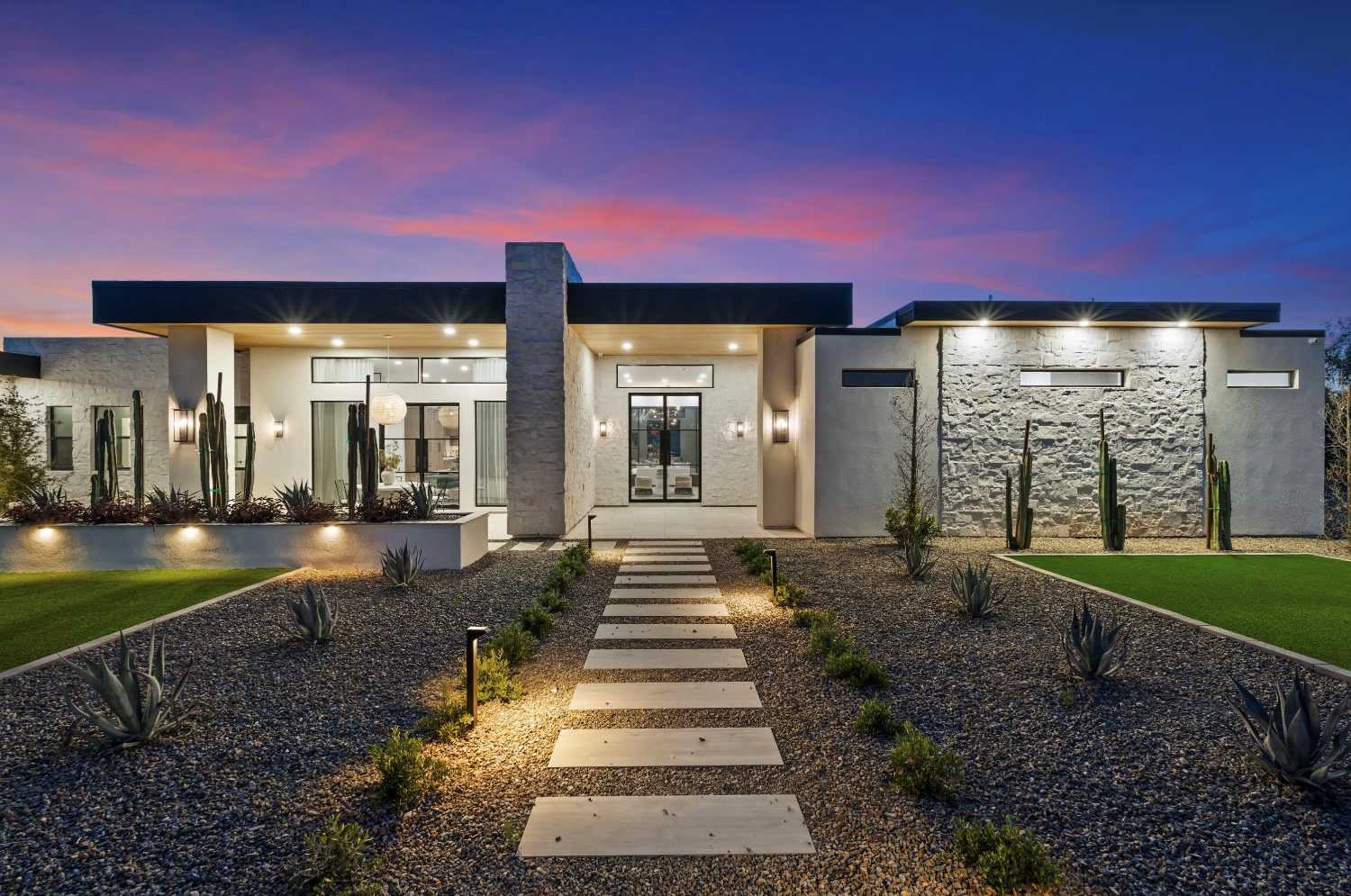 Desert-modern home at dusk with a lit stepping-stone path to glass front doors