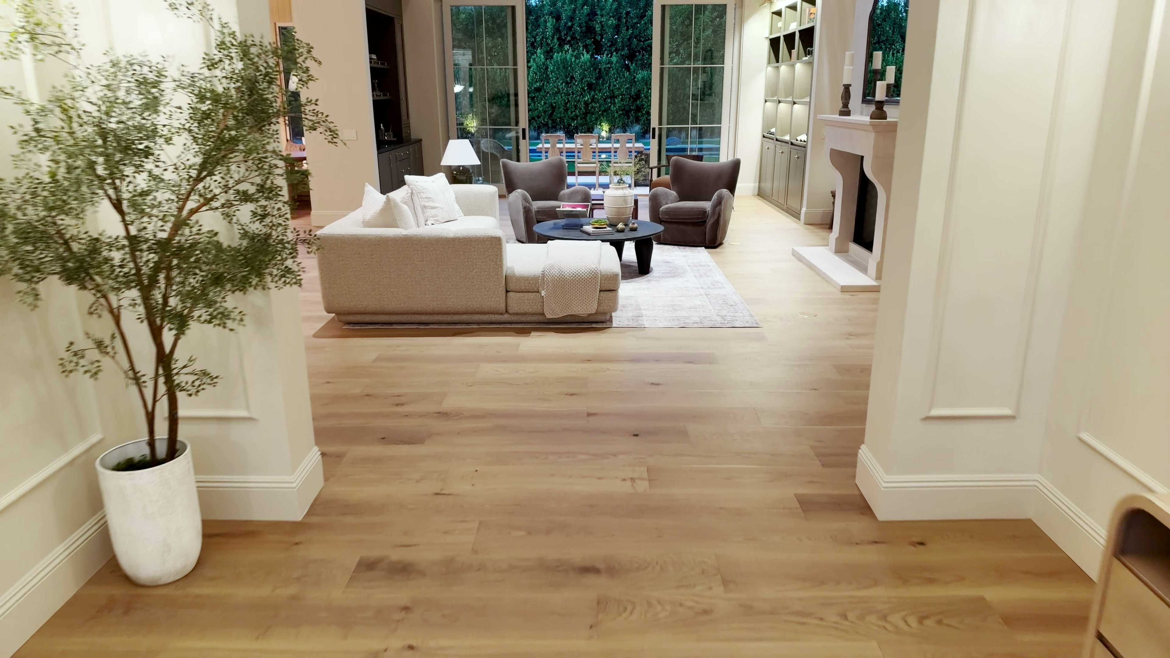 Great room seen from the entry between white columns, with a sectional sofa, a stone fireplace and glass doors to the yard